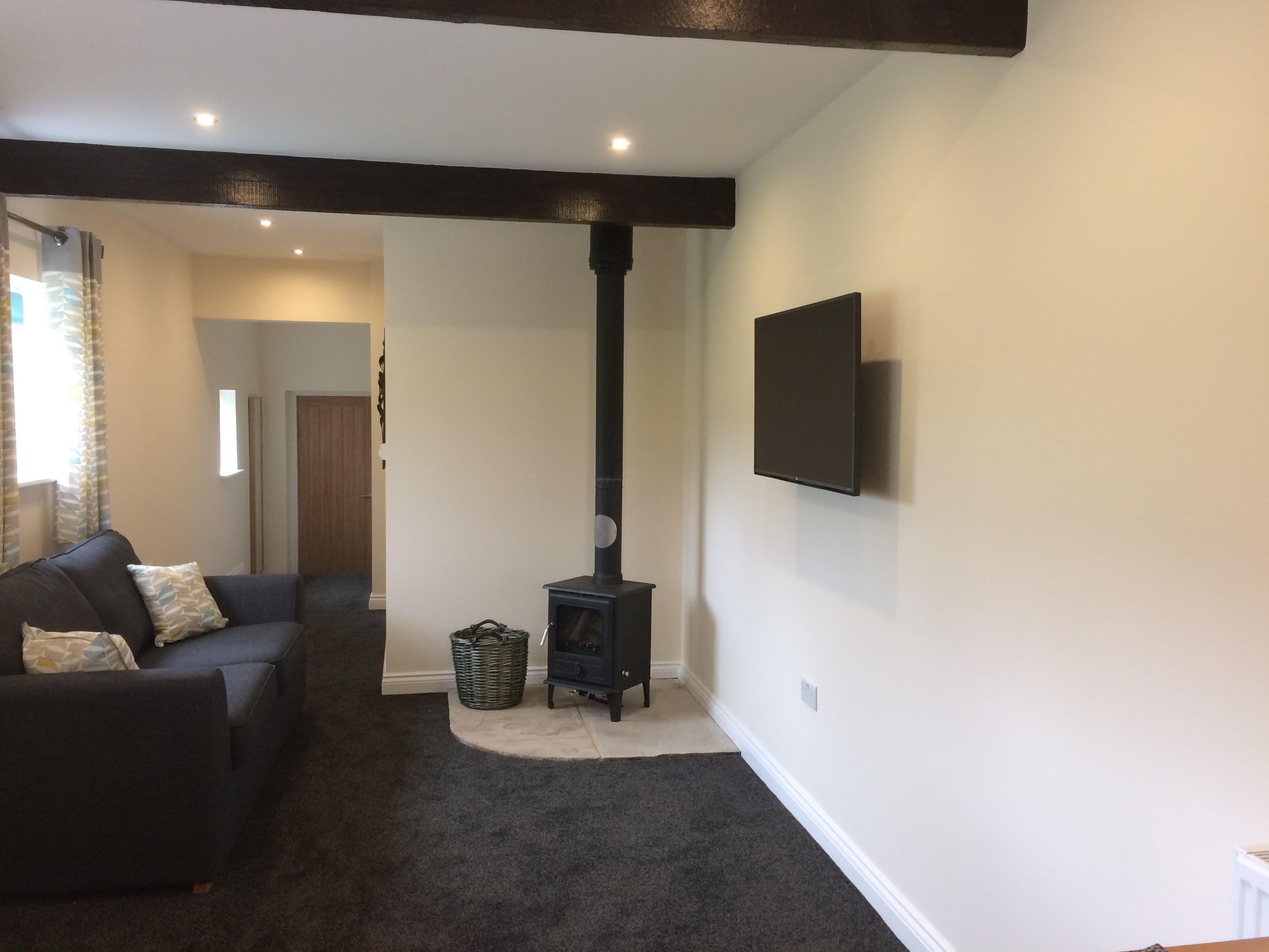 Living room area showing a comfy blue sofa, wood burning stove and HD Television